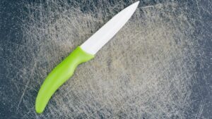 Ceramic knife with a green ergonomic handle placed on a scratched black cutting board