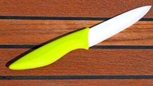 Ceramic knife with a lime green handle placed on a wooden surface with horizontal planks