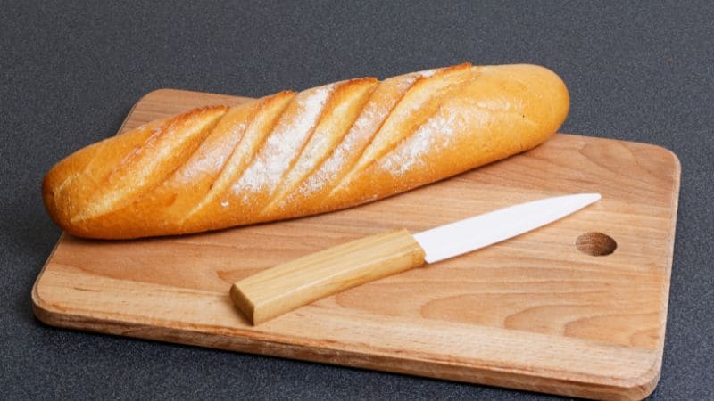 Ceramic knife with a wooden handle placed next to a fresh baguette on a wooden cutting board