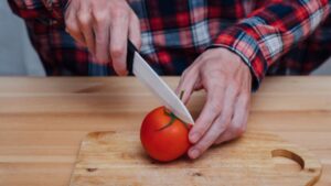 Person cutting a ripe tomato with a ceramic knife on a wooden cutting board